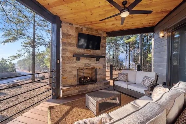 sunroom featuring an outdoor stone fireplace, wooden ceiling, and a ceiling fan