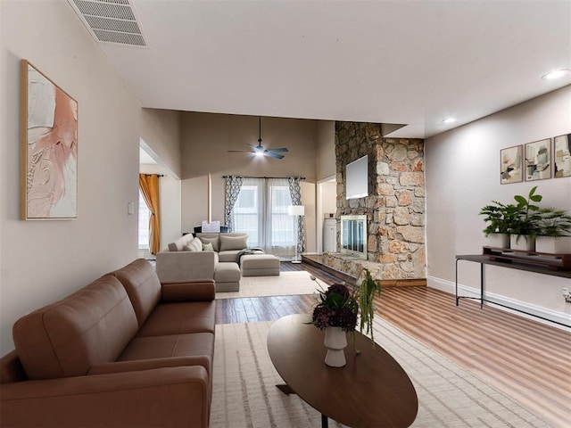 living room featuring hardwood / wood-style flooring, ceiling fan, and a stone fireplace