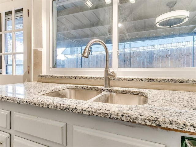 room details with white cabinetry, sink, and light stone counters