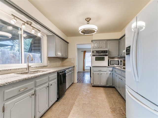 kitchen featuring gray cabinets, sink, decorative backsplash, light stone counters, and white appliances