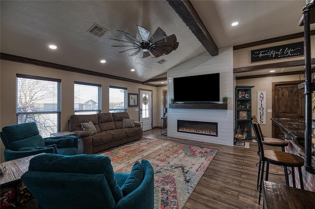 living room featuring dark wood-type flooring, vaulted ceiling with beams, crown molding, a large fireplace, and ceiling fan