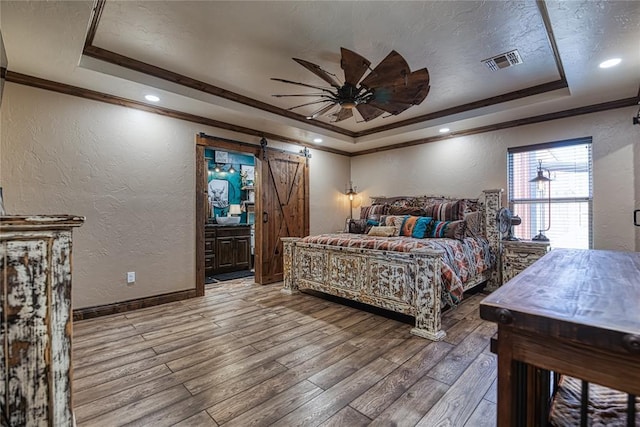 bedroom featuring wood-type flooring, a barn door, ornamental molding, and a tray ceiling