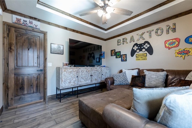 living room with ceiling fan, ornamental molding, a tray ceiling, and light hardwood / wood-style floors