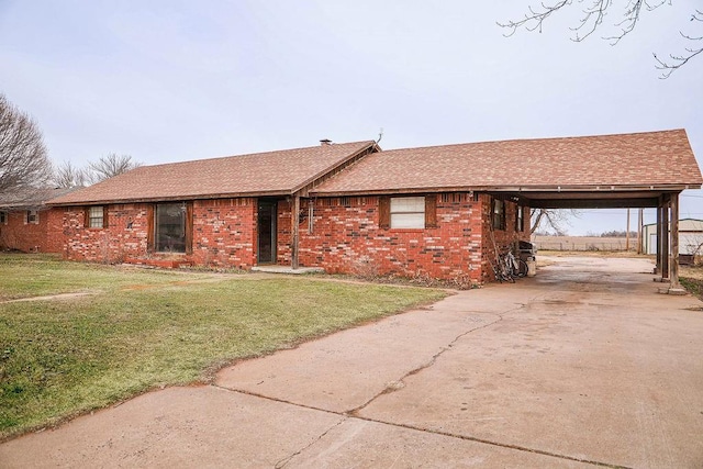 ranch-style home with brick siding, a shingled roof, concrete driveway, a front yard, and an attached carport