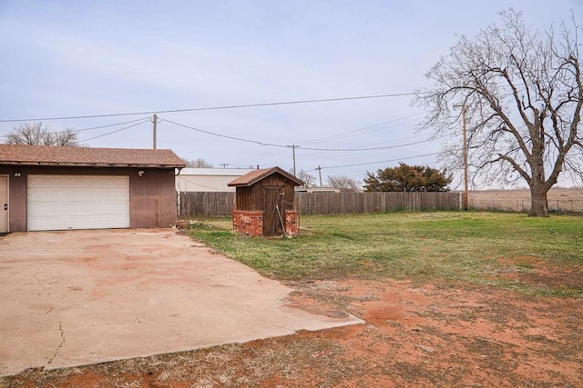 view of yard with an outbuilding, a detached garage, concrete driveway, a storage shed, and fence