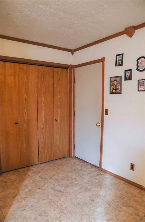 unfurnished bedroom featuring ornamental molding, a closet, a textured ceiling, and baseboards