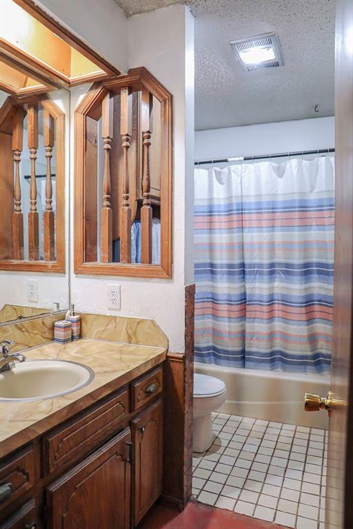 bathroom featuring visible vents, vanity, tile patterned flooring, shower / bath combination with curtain, and a textured ceiling