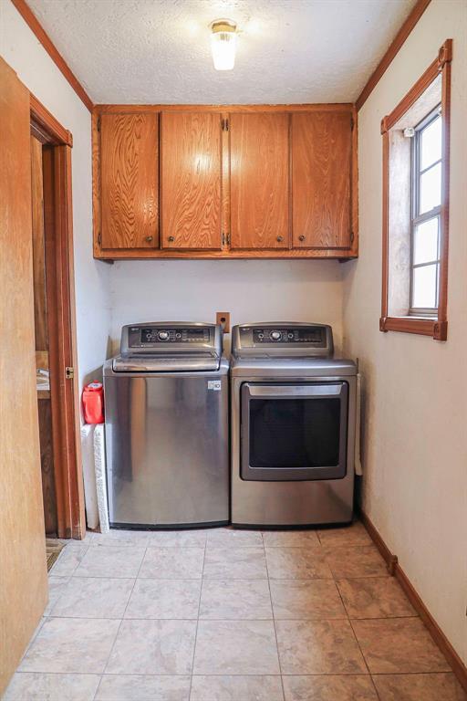 laundry room with a textured ceiling, light tile patterned floors, baseboards, washer and dryer, and cabinet space