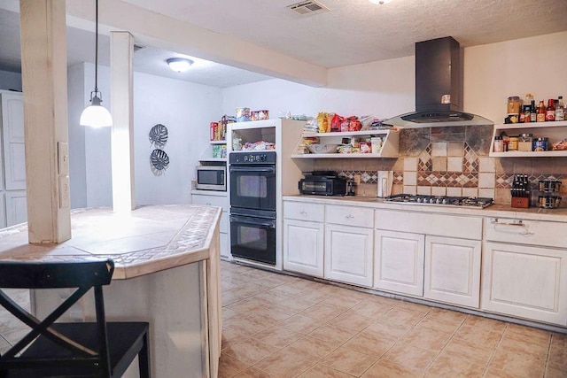 kitchen with tile countertops, stainless steel appliances, visible vents, hanging light fixtures, and ventilation hood