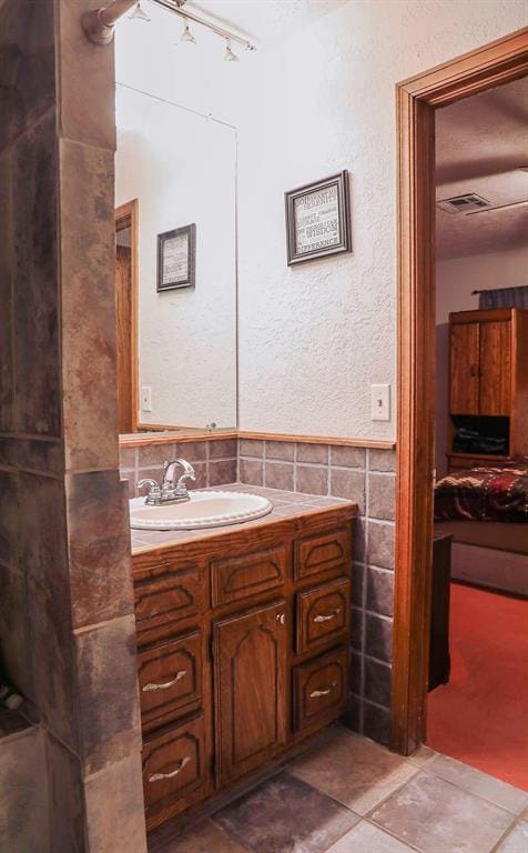 ensuite bathroom with visible vents, connected bathroom, a wainscoted wall, vanity, and tile walls