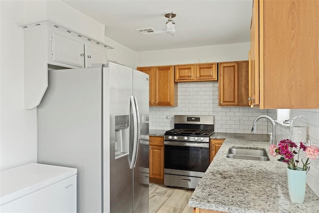 kitchen with appliances with stainless steel finishes, sink, light wood-type flooring, light stone countertops, and decorative backsplash