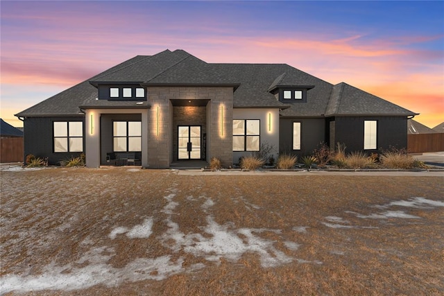 view of front of home with stucco siding, stone siding, roof with shingles, and fence