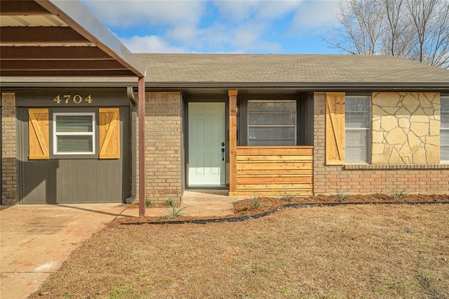 doorway to property featuring brick siding and a shingled roof