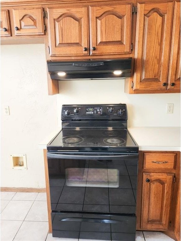 kitchen featuring light tile patterned floors, under cabinet range hood, black range with electric stovetop, baseboards, and brown cabinets