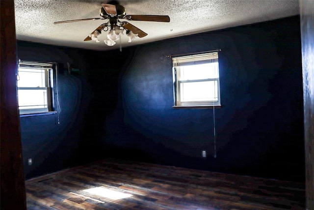 unfurnished room featuring a ceiling fan, a healthy amount of sunlight, a textured ceiling, and dark wood-type flooring