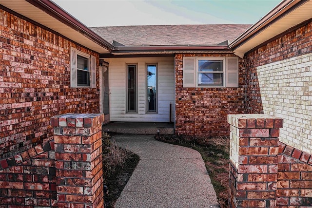 doorway to property featuring a shingled roof and brick siding