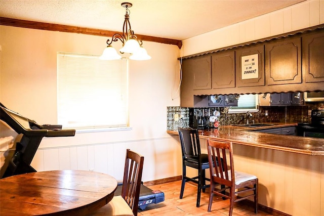 kitchen featuring dark countertops, dark brown cabinets, light wood-style flooring, black electric range oven, and pendant lighting