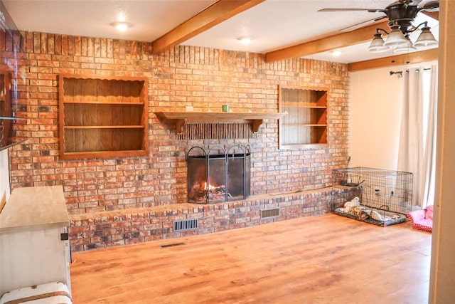 living area with a brick fireplace, visible vents, wood finished floors, and beamed ceiling