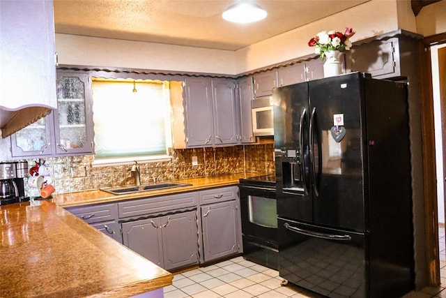 kitchen with tasteful backsplash, light tile patterned floors, a sink, black appliances, and gray cabinetry