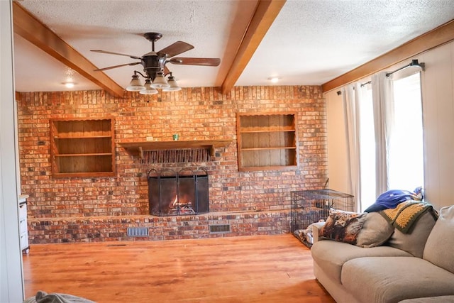 living area with visible vents, a textured ceiling, wood finished floors, and beamed ceiling