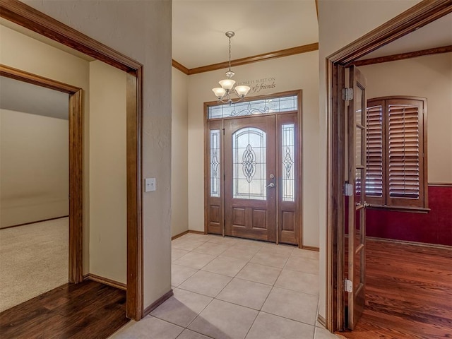 entryway with an inviting chandelier, light wood-style flooring, baseboards, and crown molding