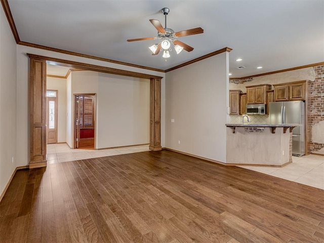 unfurnished living room with crown molding, light wood-style flooring, a ceiling fan, a sink, and baseboards