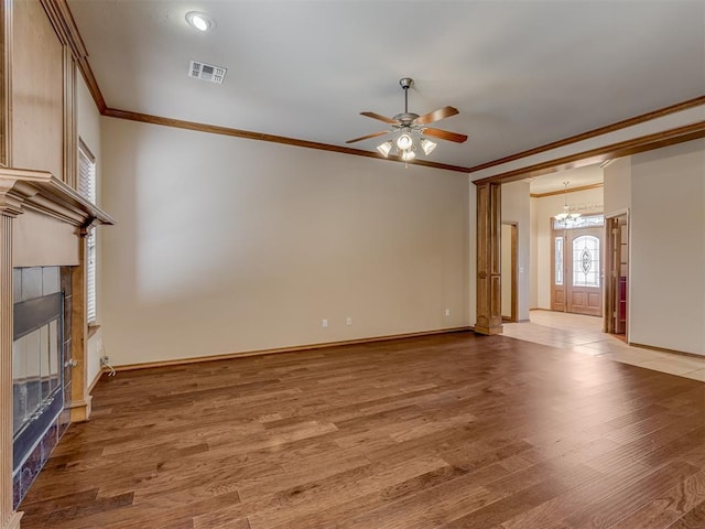 unfurnished living room featuring ornamental molding, a tiled fireplace, wood finished floors, and visible vents