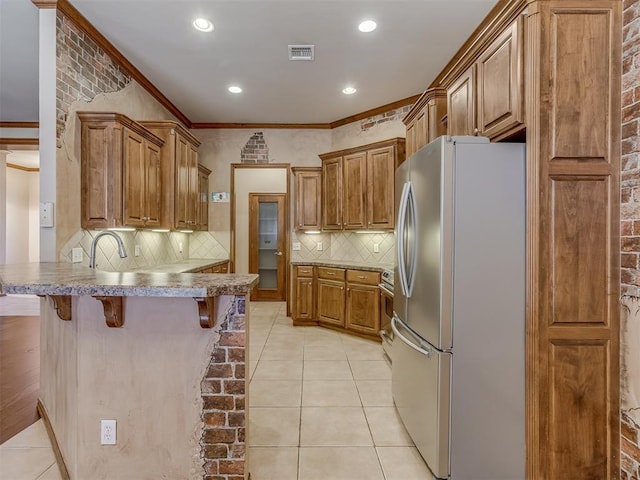 kitchen featuring light tile patterned floors, brown cabinetry, freestanding refrigerator, a peninsula, and a kitchen bar