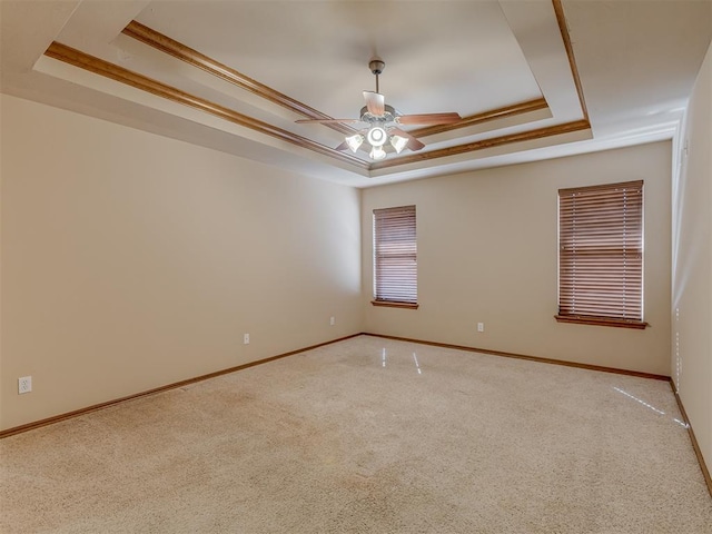 carpeted spare room with ornamental molding, a tray ceiling, a ceiling fan, and baseboards