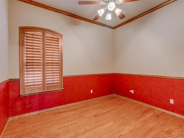 unfurnished room with a wainscoted wall, a ceiling fan, ornamental molding, and wood finished floors