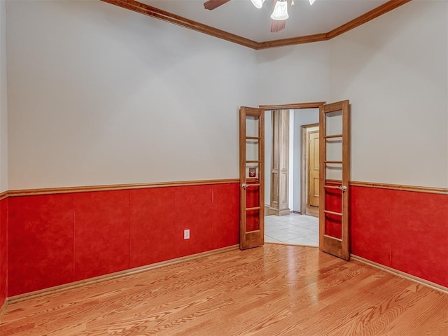 unfurnished room with crown molding, ceiling fan, wood finished floors, and wainscoting