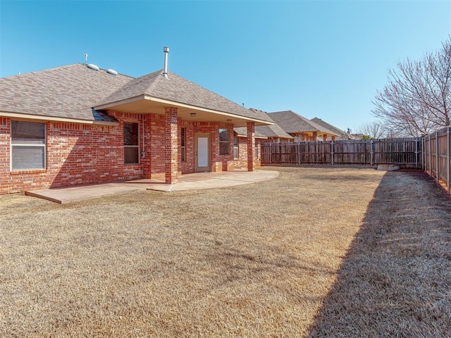 rear view of house with a fenced backyard, a lawn, a patio, and brick siding