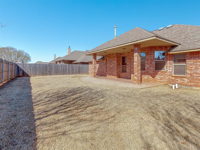 back of house with brick siding, a yard, a shingled roof, a patio area, and a fenced backyard