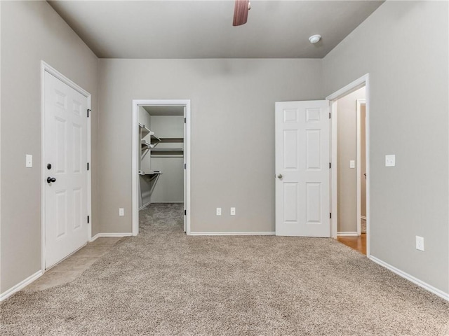 unfurnished bedroom with light carpet, ceiling fan, a closet, and a walk in closet