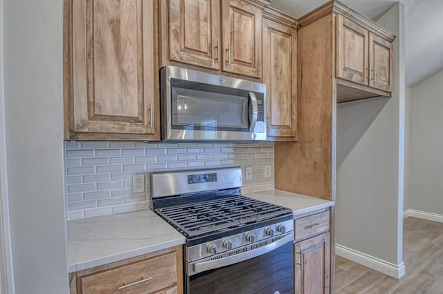 kitchen featuring baseboards, light stone countertops, decorative backsplash, appliances with stainless steel finishes, and light wood-style floors