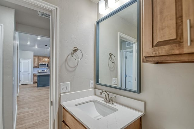 bathroom with visible vents, vanity, a textured wall, and wood finished floors