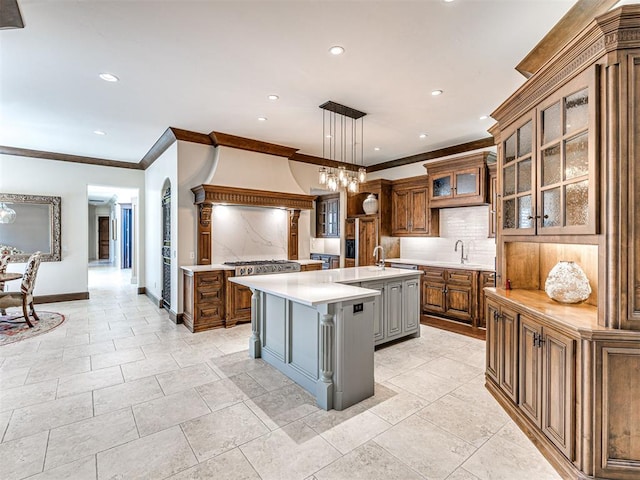 kitchen with tasteful backsplash, brown cabinetry, glass insert cabinets, light countertops, and a large island with sink