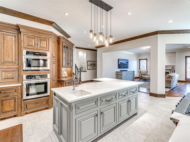 kitchen with open floor plan, gray cabinets, a center island with sink, and light stone countertops