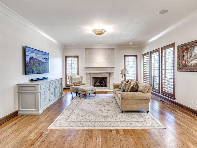 living area with light wood-style floors, baseboards, a fireplace, and ornamental molding