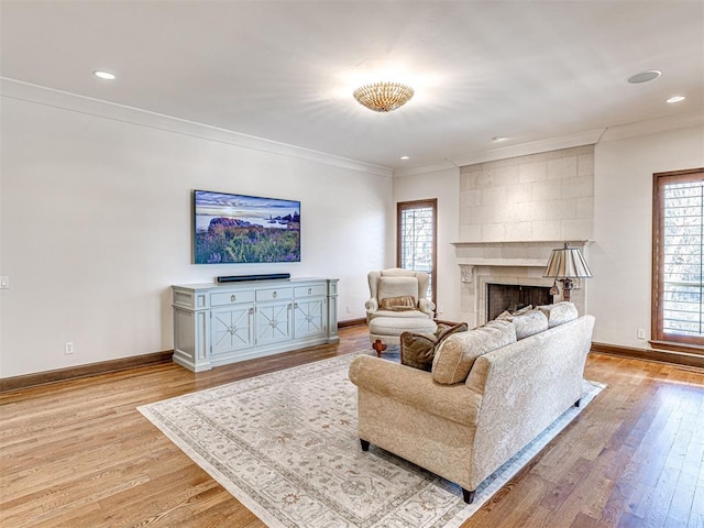 living room featuring crown molding, light wood-style floors, a fireplace, and baseboards