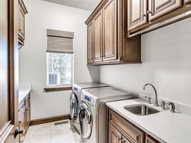 clothes washing area featuring washing machine and clothes dryer, cabinet space, visible vents, light tile patterned flooring, and a sink