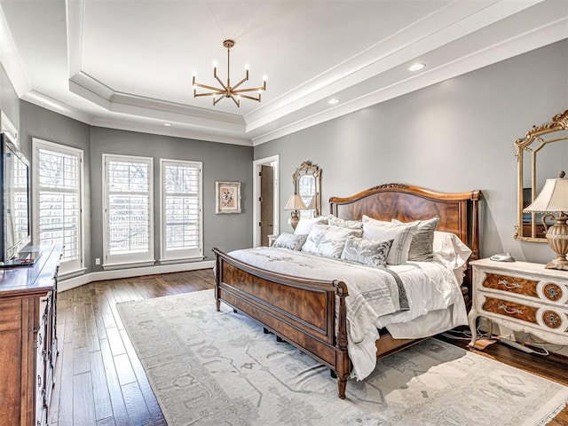 bedroom with baseboards, hardwood / wood-style flooring, ornamental molding, an inviting chandelier, and a tray ceiling