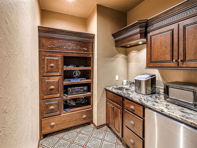 interior space with a textured wall, light stone countertops, a sink, stainless steel dishwasher, and tile patterned floors