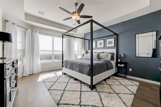 bedroom with a raised ceiling, visible vents, baseboards, and wood finished floors