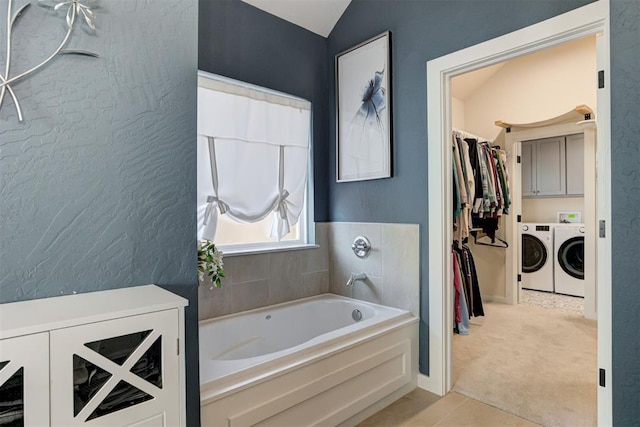 bathroom with a textured wall, a garden tub, vaulted ceiling, independent washer and dryer, and a walk in closet