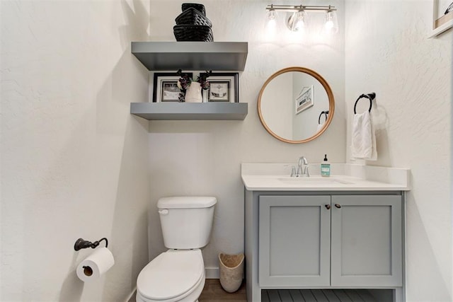 half bath featuring a textured wall, vanity, and toilet