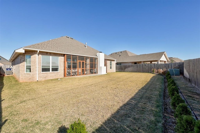 rear view of house featuring a shingled roof, a lawn, a sunroom, a fenced backyard, and brick siding