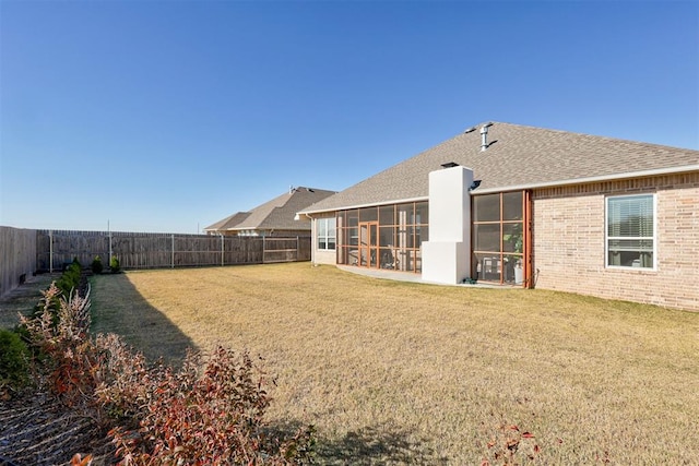 rear view of house with a fenced backyard, brick siding, a sunroom, roof with shingles, and a lawn