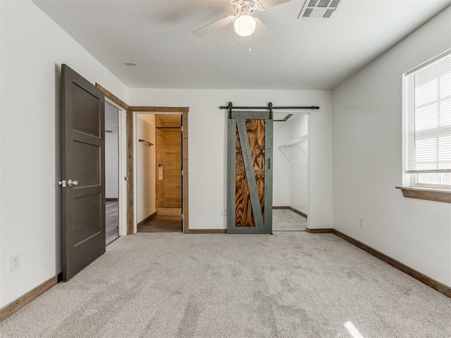 unfurnished bedroom featuring light colored carpet, ensuite bath, a barn door, a closet, and a spacious closet