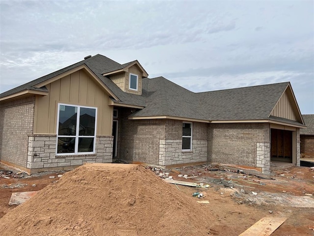 view of front facade featuring roof with shingles, brick siding, and board and batten siding